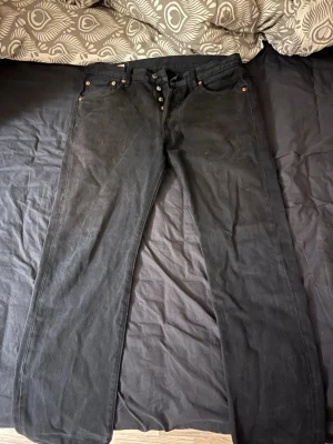 Svarta Levi's raka jeans - Säljer ett par svarta jeans från Levi's med rak passform och klassisk femficksdesign. Jeansen har knappgylf och detaljer i metall. Tillverkade i slitstark denim med Levi's ikoniska läderpatch bak i midjan och röd logotagg på bakfickan. Ny pris 1200kr men säljer dessa nu för 400kr! Priset är inte hugget i sten så kom med förslag!