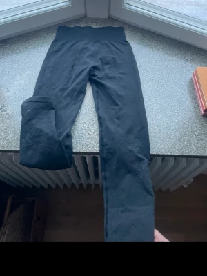 Svarta ribbade träningstights - Svarta träningstights med ribbad struktur och hög midja. Tightsen är stretchiga och sitter tight, perfekta för gym eller löpning. Materialet känns mjukt och följsamt, troligtvis en blandning av syntet och elastan. Inga synliga loggor eller märken.