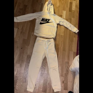 Beige Nike tracksuit - Snygg beige hoodie från Nike med stor svart logga på bröstet. Hoodien har huva med vit dragsko och är gjord i mjukt material, perfekt för en avslappnad streetstyle-look. Passar xs, helt oanvänd 