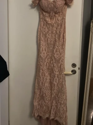 Lång spetsklänning i ljusrosa - Romantisk långklänning i ljusrosa spets med offshoulder,Klänningen har vacker broderad spets, paljettdetaljer och figurnära passform. Perfekt för bal eller fest. Materialet känns lyxigt och elegant. Och har fina knappar nertill på baksidan 😍
