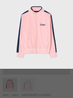 Rosa zip hoodie med blå ränder - Snygg rosa hoodie med dragkedja från Djurgårdsbutiken . Tröjan har mörkblå ränder längs ärmarna och en liten broderad logga på bröstet. Tillverkad i mjukt material och har ribbade muddar vid ärmslut och nederkant. Perfekt för en sportig och avslappnad stil. Original pris 800kr