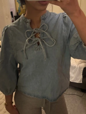 Ljusblå jeansblus med knytning - Ljusblå jeansblus med trekvartsärm och snygg knytning framtill. 