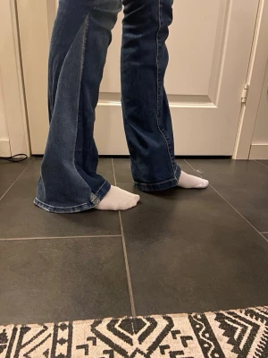 Blå bootcut jeans med slitningar - Säljer ett par blå bootcut jeans med lätt slitna detaljer på framsidan. Jeansen har en klassisk femficksmodell och är tillverkade i denim med en snygg tvätt. Perfekta för dig som gillar en retroinspirerad look med utsvängda ben. Midjemått 37, Innerbenslängd 84. Storlek 28/34💕