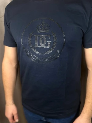 Mörkblå Dolce & Gabbana t-shirt - Snygg mörkblå t-shirt från Dolce & Gabbana med ett stort, glansigt logotryck på bröstet. T-shirten har rund hals och korta ärmar. Tillverkad i mjuk bomull som känns skön mot huden. Perfekt för dig som gillar exklusiva märken och stilren design.