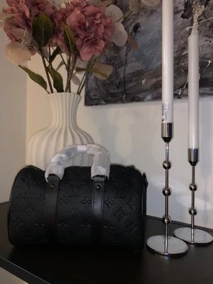 Svart monogram handväska Louis Vuitton - Snygg svart handväska från Louis Vuitton med klassiskt monogrammönster i präglat läder. Väskan har rundad form, dubbla handtag och detaljer i svart. Perfekt för dig som vill ha en lyxig och trendig accessoar.