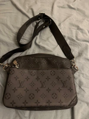 Louis Vuitton monogram axelväska - Snygg axelväska från Louis Vuitton i mörkbrunt med klassiskt monogrammönster. Väskan har justerbar bred axelrem i svart textil och detaljer i silverfärgad metall. Tillverkad i tåligt canvasmaterial med dragkedja upptill och stilren, modern look. Kan diskutera pris.