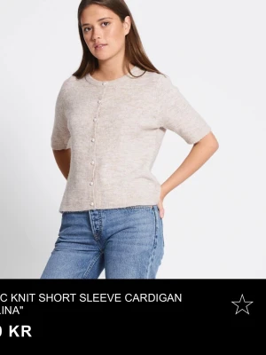 Beige kortärmad stickad kofta - Kortärmad stickad kofta i beige med rund hals och pärlemorknappar framtill. Koftan har en rak passform och ribbade kanter. Perfekt att styla med jeans eller kjol för en avslappnad look. Jag har endas använd denna 2 gånger så den är i fint skick. Nypris 150💕