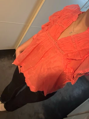 Korallrosa blus med volanger - Snygg korallrosa blus med volangdetaljer och v-ringning från Neo Noir.