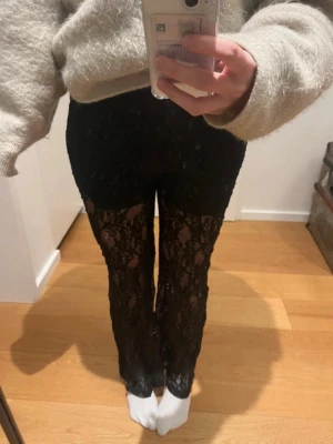 Svarta spetsbyxor med utsvängda ben - Säljer ett par svarta byxor i genombruten spets med  utsvängda ben. De har ett snyggt blommigt spetsmönster och är perfekta för dig som vill sticka ut. Materialet är stretchigt och följsamt. Passar till både chill och mer dressade looks. Storlek L men passar mer M skulle jag säga. 