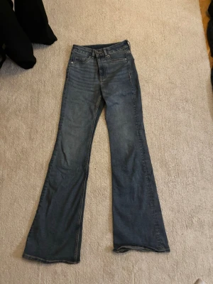 Blå bootcut jeans med hög midja - Säljer ett par blå bootcut jeans med hög midja och klassisk femficksmodell. Jeansen har en snygg tvätt och vida ben som ger en retrovibe. Perfekta att styla med sneakers eller boots för en cool look.