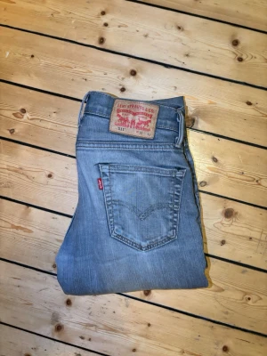 Levi's ljusblå raka jeans - Säljer ett par klassiska ljusblå jeans från Levi's med raka ben och femficksmodell. Jeansen har den ikoniska röda Levi's-lappen på bakfickan och patch i läder bak i midjan. Tillverkade i slitstark denim, perfekta för en avslappnad och tidlös stil.