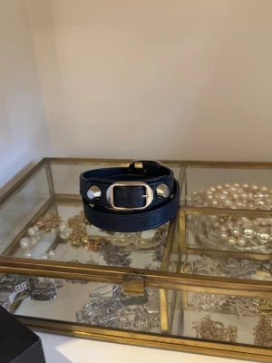 Balenciaga Classic Triple Tour läderarmband - mörkblå färg  - Balenciaga Classic Triple Tour läderarmband i mörkblå färg med silverfärgade nitar och spänne.  Jag köpte det på Vestiaire collective för ungefär 2 år sedan och har inte använt det mer än 3 gånger. Äkthetskoden och "Balenciaga"-märket finns på bild 5. Tyvärr har jag inte kvittot (vilket förklarar priset).  - Skick: mycket bra, lätt repade nitar (se bild 6) - Mått: längd cirka 52 cm  - Material: Läder   Vänligen meddela mig om du behöver ytterligare information💌