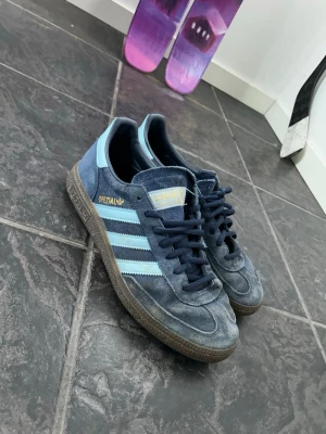 Adidas Spezial blå sneakers - Säljer ett par Adidas Spezial sneakers i blå mocka med ljusblå ränder och detaljer. Skorna har inte används mycket alls max 3 gånger sommaren 2025. Jag slutade använda dom för det var inte riktigt min stil så de är helt oanvända typ. Inga slitningar alls på dom. Kanske nån fläck men går att få bort lätt med vatten bara. Syns knappast. Du får även med kartongen. Skorna är köpa från JD sport.