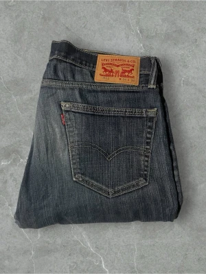 Levi's 511 blå jeans W34 L34 - Säljer ett par klassiska Levi's 511 jeans i blå denim med snygg tvätt och raka ben. Jeansen har fem fickor, tydliga kontrastsömmar och den ikoniska läderlappen bak i midjan. Perfekta för dig som gillar tidlös stil och vill ha ett par jeans som alltid funkar.