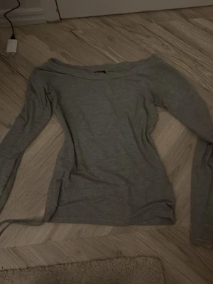 Grå offshoulder topp - Säljer en enkel och stilren grå offshoulder topp med lång ärm. Toppen har en smal passform och är tillverkad i mjukt material som känns skönt mot huden. Perfekt att matcha med jeans eller kjol för en clean look.