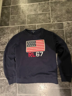 Tröja från Ralph Lauren med amerikansk flagga - Mörkblå tröja från Polo Ralph Lauren med amerikansk flagga. Bra skick och perfekt för en avslappnad stil. Står XL men passar M