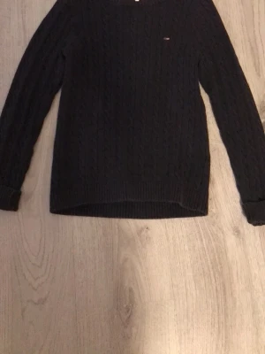 Mörkblå kabelstickad tröja Lexington - Kabelstickad mörkblå tröja från Lexington med rund halsringning och diskret logga på bröstet. Tröjan har långa ärmar och ribbade muddar vid ärmslut och nederkant. Perfekt för en klassisk och stilren look.