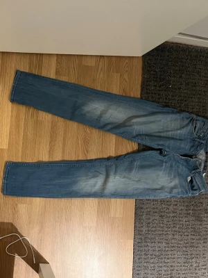 Blå raka jeans från Replay - Säljer ett par klassiska blå jeans från Replay med raka ben och snyggt slitna detaljer på framsidan. Jeansen har fem fickor och en läderpatch bak i midjan. Perfekt för dig som gillar tidlös denimstil.