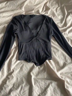 Svart långärmad korsettopp  - Trendig svart långärmad topp från Aim'n med korsett-inspirerad midja och djup v-ringning. Toppen har markerade sömmar framtill som ger en snygg siluett och är perfekt för att lyfta vilken outfit som helst.