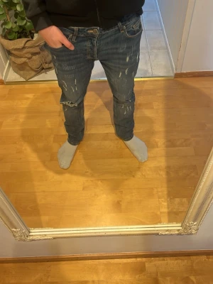 Blå slitna jeans med distressed detaljer - Säljer nu dessa riktigt feta jeans med snygga slitningar och distressed detaljer på både fram- och baksida. Jeansen har slim fitt passform, fem fickor och klassisk knappgylf. Perfekta för en avslappnad och trendig look.
