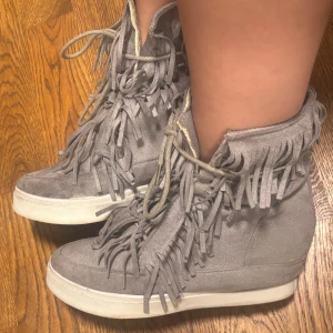 Grå fransskor med kilklack  - Säljer ett par supersnygga Isabell marant liknande grå fransskor med kilklack på ca 4 cm. De är jättebekväma att gå i och passar lika bra till jeans som till klänning. Endast använda en gång i mycket fint skick.