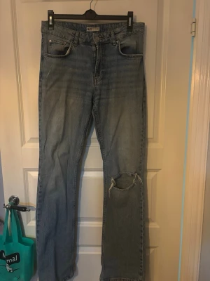 Ljusblå raka jeans från Gina Tricot - Säljer ett par ljusblå raka jeans från Gina Tricot med slitning och hål på ena knät. Klassisk femficksmodell med dragkedja och knapp. Perfekta för en avslappnad och trendig look.