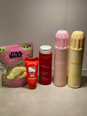 Skönhetspaket med duschskum, handkräm och bathbombs - Ett färgglatt skönhetspaket med Sundae duschskum i dofterna Birthday Cake(använts 1gång) och Honey Honey (använts 2ggr), Clarins duschgel (ca hälften kvar) , Hello Kitty handkräm som luktar jordgubb (använts 2ggr) och Star Wars Mandalorian badbomb (4st). Perfekt för dig som gillar söta dofter och roliga förpackningar.