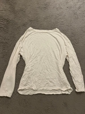 Vit långärmad topp - En enkel och stilren vit långärmad topp med rund halsringning. Tillverkad i mjuk bomull som känns skön mot huden. Perfekt att matcha med jeans eller kjol för en clean look. Aldrig använd, bara provad. Jag är osäker på storleken men tror det är storlek s, skulle kunna vara storlek m då den är oversized på mig som brukar ha s.