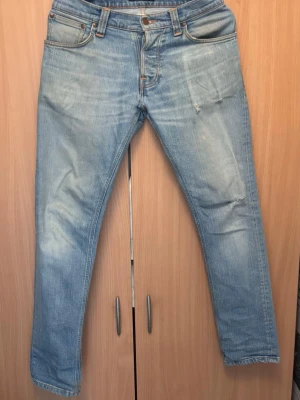 Ljusblå raka jeans från Nudie - Säljer ett par ljusblå jeans med små slitningar på knäna och låren från Nudie. Materialet är mjuk denim i bomull. W29, L32