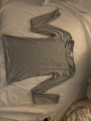 Grå ribbad långärmad topp H&M - En enkel och stilren grå långärmad topp från H&M i ribbad bomullsmix. Modellen är figurnära med rund halsringning och passar perfekt till jeans eller kjol. Superenkel att matcha och ett måste i basgarderoben.