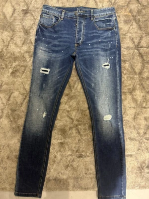 Blå slitna skinny jeans - Snygga blå skinny jeans med slitningar och distressed detaljer på framsidan. Jeansen har klassisk femficksmodell, normal midja och är tillverkade i denim med lätt stretch. Perfekta för en avslappnad och trendig look.
