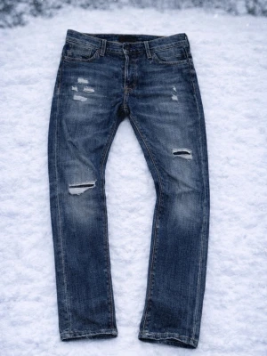 Jack and Jones jeans med slitningar 30L/30W - Ett par feta Jack and Jones jeans med sköna slitningar som är gjorda originellt. Ett perfekt val för ett par lite mer vintage jeans!
