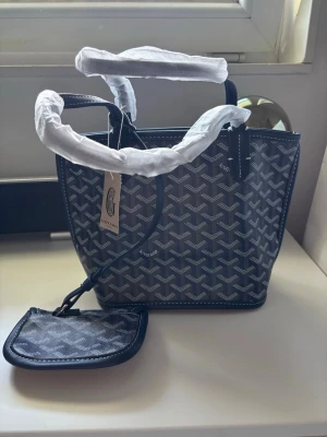 Marinblå handväska med mönster - Snygg marinblå handväska  med klassiskt vitt mönster och matchande liten pouch. Väskan har två handtag och är tillverkad i canvas med läderdetaljer. Perfekt för dig som gillar exklusiva accessoarer och vill sticka ut med en ikonisk design.