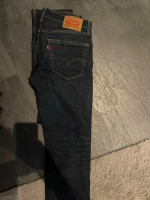 Mörkblå Levi's jeans straight fit - Säljer ett par mörkblå jeans från Levi's med klassisk straight fit och femficksmodell. Jeansen har kontrastsömmar, läderpatch bak och Levi's röda etikett på bakfickan. Perfekta till en avslappnad stil och tillverkade i slitstark denim.