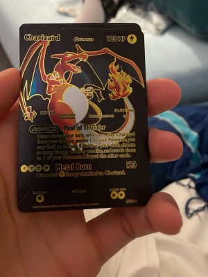 Charizard Pokémonkort svart/guld - Säljer ett Charizard Pokémonkort i svart och guld med holografiska detaljer. Kortet har en cool design med Charizard i centrum och text i guld. Perfekt för samlare eller dig som vill ha ett unikt kort till din samling.