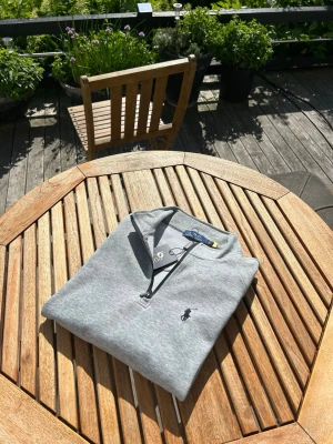 Grå half zip tröja från Polo Ralph Lauren - Snygg grå långärmad tröja från Polo Ralph Lauren med half zip och klassisk broderad logga på bröstet. Perfekt till chill vardagsstil och enkel att matcha med jeans eller chinos. Mjuk bomullskvalitet för extra komfort.