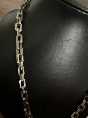 Kedjehalsband i silverfärgad metall - Säljer ett stilrent halsband med rektangulära länkar i silverfärgad metall. Kedjan har en modern och robust design som passar perfekt till en trendig look. Inget synligt märke på halsbandet. Perfekt accessoar för dig som gillar minimalistisk stil.