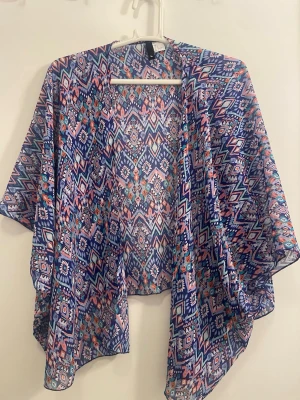 Mönstrad bolerotopp i polyester - Färgglad bolerotopp med korta ärmar och ett snyggt geometriskt mönster i blått, rosa och vitt. Tillverkad i 100% polyester, luftig och perfekt för varmare dagar. Öppen framtill och loose passform för en avslappnad stil.