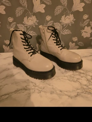 Beige chunky kängor med snörning - Säljer ett par beige chunky kängor med svart platåsula och snörning framtill. Kängorna har dragkedja på sidan för enkel på- och avtagning och är tillverkade i ett slätt material som liknar skinn. Perfekta för dig som vill ha en edgy stil.