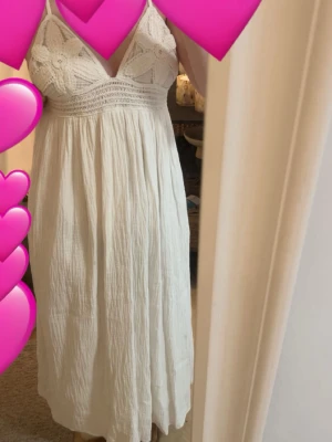 Vit långklänning med virkade detaljer - Supersöt vit långklänning med virkade blommor upptill och tunna axelband. Överdelen har en omlottkänsla och kjolen är i ett mjukt, luftigt tyg (muslin tyg) som faller snyggt. Perfekt för varma dagar och sommarvibbar. ‼️***OBS!!! Dragkedjan är tyvärr sönder!!*****‼️ Den har liksom hoppat ur och jag har tänkt gå till en skräddare och fixa men glömt bort och nu är klänningen för liten tyvärr, använd 1 gång..🫧🤍 Klänningen kan ej köpas längre. Klänningen har justerbara band💓