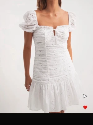 Vit kort klänning med puffärm - Superfin vit kort klänning med puffärmar och broderade spetsdetaljer. Klänningen har fyrkantig urringning, liten rosett framtill och volang nedtill. Perfekt för sommarens alla tillfällen och ger en romantisk vibe.