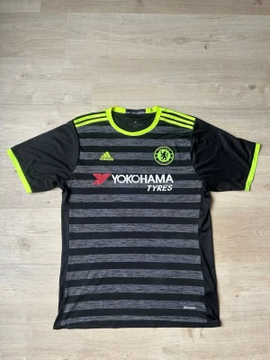 Svart Chelsea FC Fotbollströja Borta 2016/17 Storlek XL - Mycket fin fotbollströja i svart färg. Tröjan är i mycket bra skick och sparsamt använda. |  Äkta som allt annat jag säljer! ✅ |  Storlek: XL | Skick: Bra Skick - Tyvärr har trycket börjat släppt litegrann på baktrycket och sponsortrycket (SE SISTA BILD) | Färg: Svart | Märke: adidas | Modell: Fotbollströja |   Hör gärna av dig vid frågor så svarar jag s