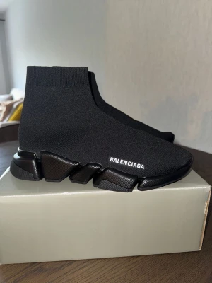 Balenciaga Speed Trainer svarta sneakers - Svarta Balenciaga Speed Trainer sneakers med stickad ovandel i stretchigt tyg och chunky sula. Loggan är tryckt i vitt på sidan. Skorna har en strumpliknande passform och futuristisk design som sticker ut.