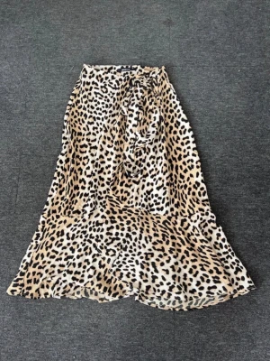 Leopardmönstrad omlottkjol Gina Tricot - Säljer en lång leopardmönstrad omlottkjol från Gina Tricot. Kjolen har volangkant nertill och knytband i midjan. Färgerna är beige, svart och brun, och materialet känns lätt och flowy, perfekt för att sticka ut. Passar som en S också