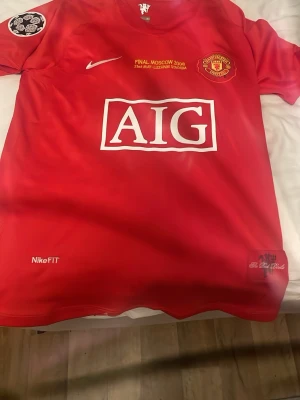 Manchester United finaltröja Nike Ronaldo - Röd Manchester United matchtröja från Nike med AIG som sponsor, klubbmärke och Champions League-märke på ärmen. Tryck för finalen i Moskva 2008 på bröstet. Tillverkad i NikeFIT-material för bra komfort under träning eller match.