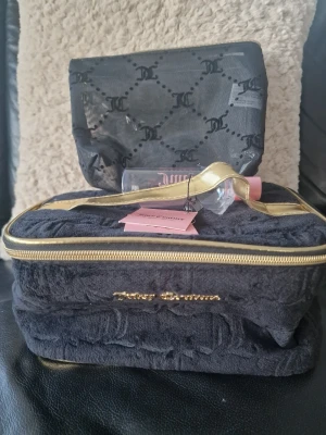 Juicy Couture svart necessärset - Juicy Couture necessärset i svart med guldiga detaljer. Stora väskan är i mjuk velour med präglad logga och guldfärgad dragkedja. Mindre väska i genomskinlig plast med svart JC-mönster. Perfekt för smink eller småprylar.