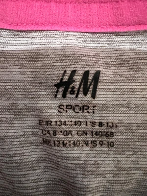 Grå sportig topp från H&M - En gråmelerad sporttopp från H&M med enkel, ärmlös design och rund hals. Perfekt för träning eller chill dagar. Materialet är mjukt och stretchigt, vilket ger en bekväm passform.