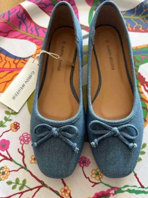 Blå ballerinaskor från Carin Wester - Snygga blå ballerinaskor från Carin Wester i denimliknande tyg. Skorna har rund tå och en söt rosett framtill. Perfekta för dig som gillar en avslappnad men trendig stil. Innerdelen är beige och de har en klassisk ballerinamodell. Helt nya, prislapp är kvar! 