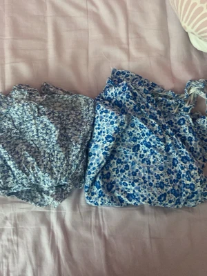 Blommiga blå tubtoppar - Två söta blommiga tubtoppar i olika blå nyanser. Ena toppen har smockad struktur och småblommigt mönster, den andra har större blå blommor och knytband upptill. Perfekta för sommaren och lätta att matcha med jeans eller kjol.