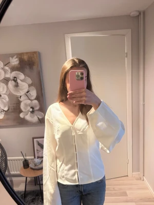 Vit blus med vida ärmar och knappar - Aldrig använd. Helt ny med prislapp kvar. Stilren vit blus med djup V-ringning. Blusen har långa, vida ärmar. Perfekt att matcha med jeans eller kjol. 